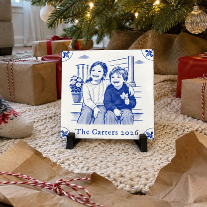 A Delft-blue photo tile on its stand under a Christmas tree, just unwrapped from kraft paper