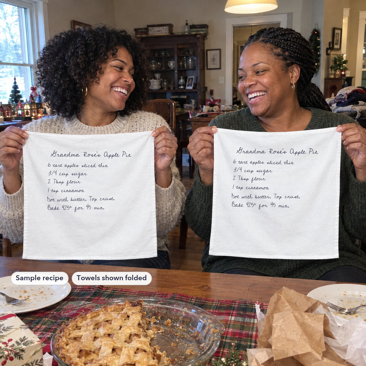 Two sisters holding up matching recipe tea towels, shown folded, at a holiday table (sample recipe)
