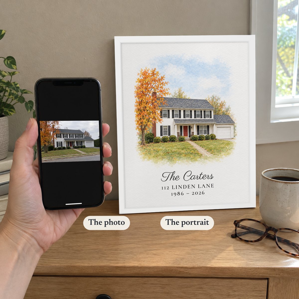 A hand holding a phone with the original photo of the house next to the white-framed portrait made from it