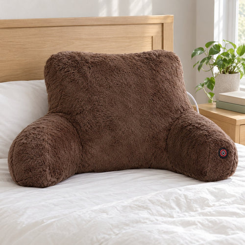 Brown faux fur heated backrest pillow with armrests standing on a made bed, power button on the right armrest