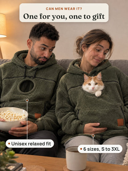 A couple on the sofa in matching olive cat pouch hoodies, the cat peeking out of hers while he pretends to be jealous