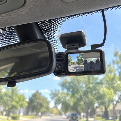 The dash cam mounted on the windshield behind the rear-view mirror, screen and cabin lens facing inside
