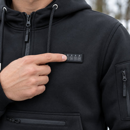 Finger pressing the power button patch on the chest of the heated hoodie, next to the quarter-zip