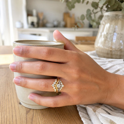 Gold ring jacket worn around a dainty engagement ring, holding a coffee