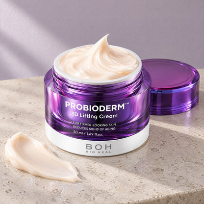 Open violet jar of 3D Lifting Cream with a swirl of whipped ivory cream on a stone bathroom counter