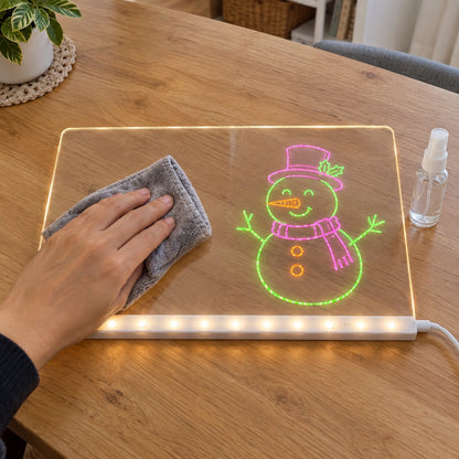Hand wiping a glowing snowman drawing off the clear board with a grey cloth, spray bottle next to it