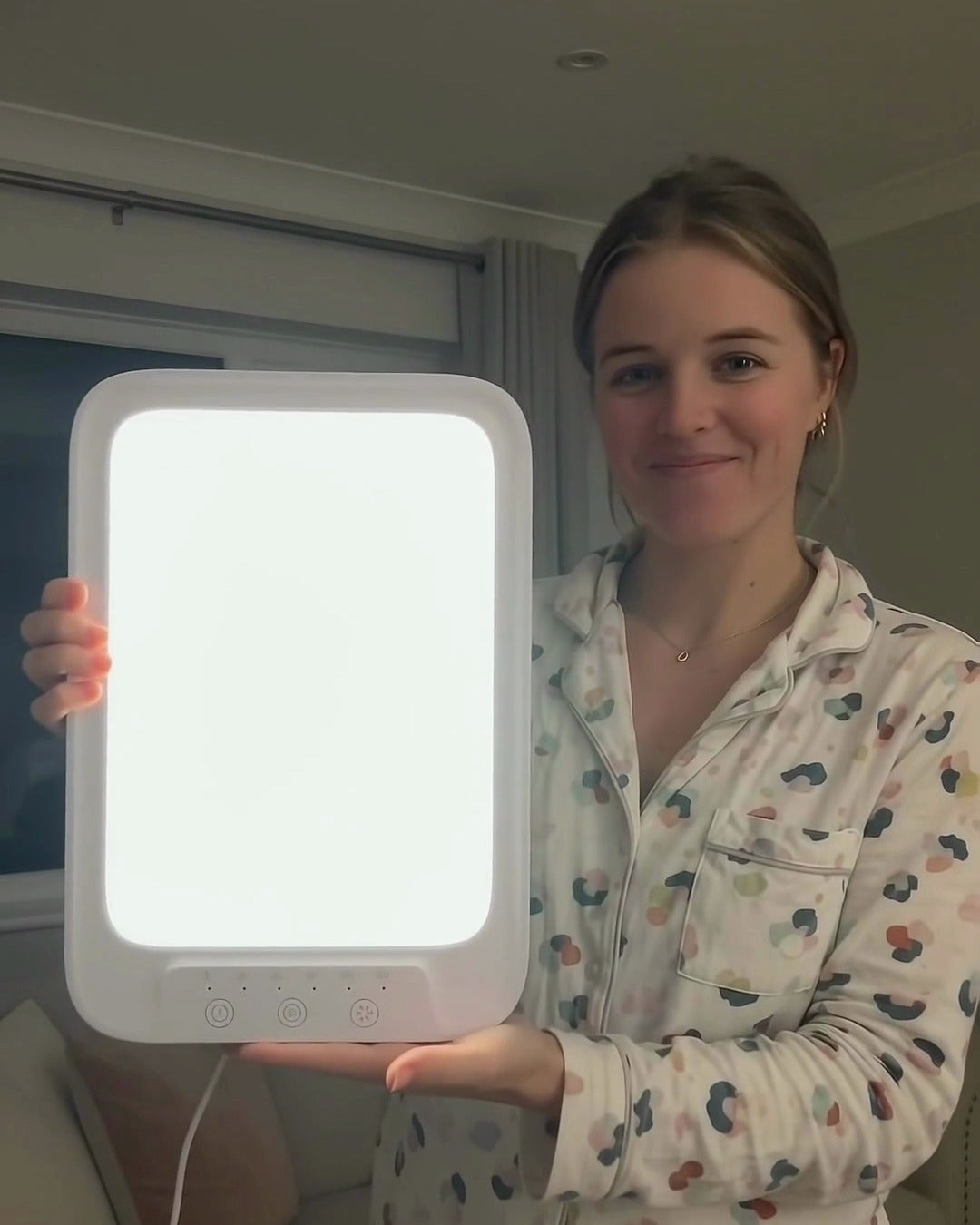 Woman in pajamas holding the glowing light therapy lamp toward the camera