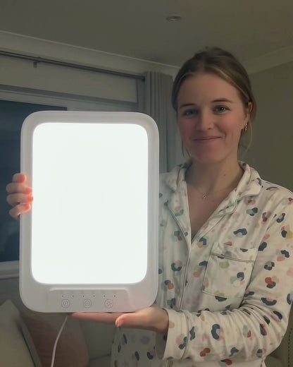 Woman in pajamas holding the glowing light therapy lamp toward the camera