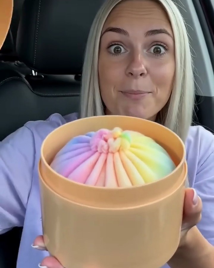 Creator holding the open steamer box with the rainbow plush inside, frame from her video