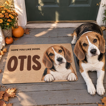 Doormat printed with a beagle named Otis and the words Hope you like dogs, in front of a green front door, with the real beagle lying beside it