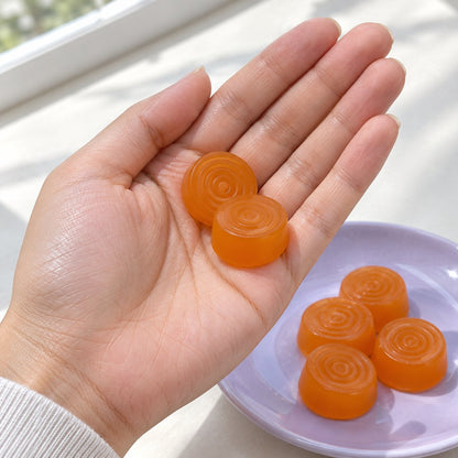 Two orange pineapple probiotic gummies in a woman's hand