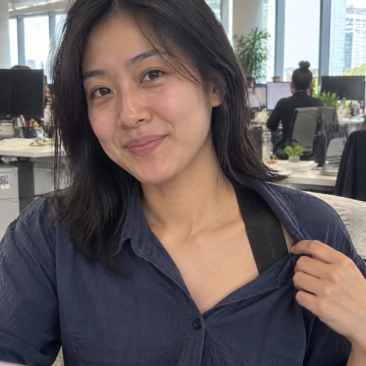Woman at her desk pulling her shirt collar aside to show the black strap underneath