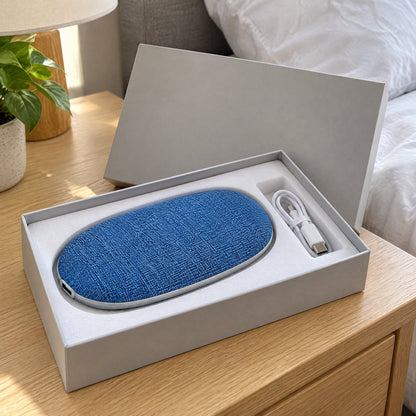 The under-pillow speaker in its gift box with a charging cable, on a nightstand