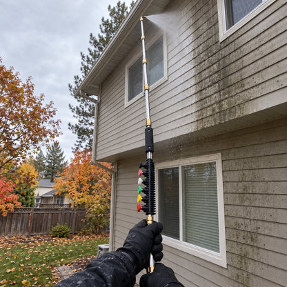 View from the ground: hands holding the extension wand straight up the wall, spraying grime off second-story vinyl siding