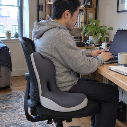 Man working at a home desk on an office chair fitted with the seat and lumbar cushion