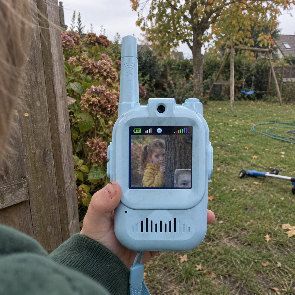 A boy hiding behind a backyard fence sees his sister on the walkie-talkie screen