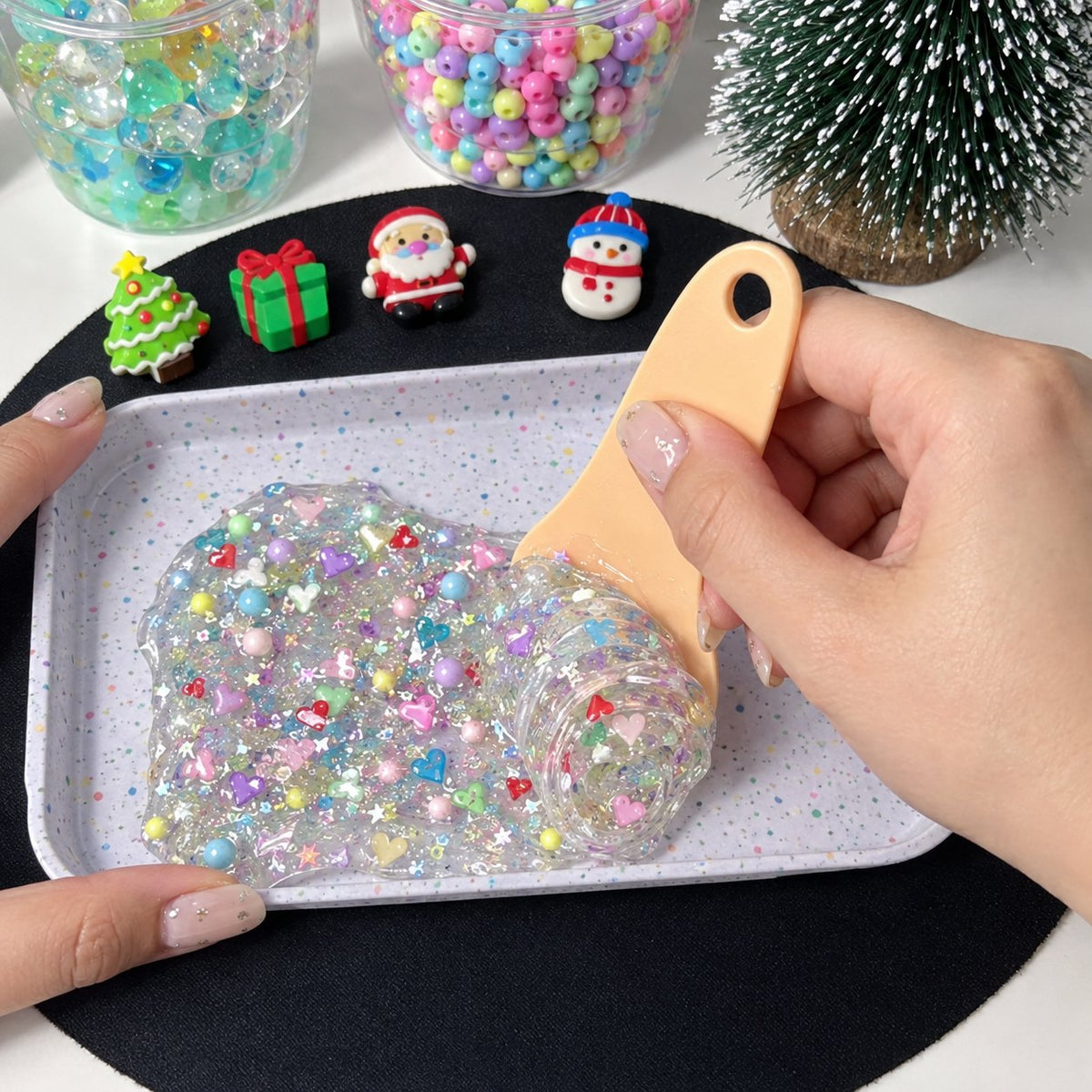Hand rolling clear gel with beads and heart confetti on a tray with a scraper