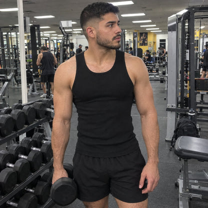 Man at the gym in the black fitted tank, holding a dumbbell