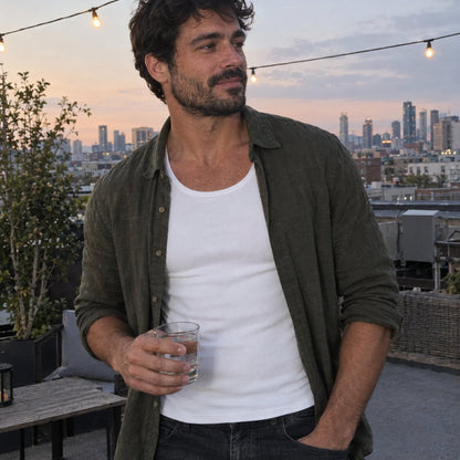Man on a rooftop in the evening wearing the white tank under an open olive shirt
