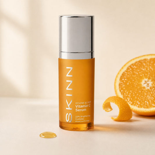 Vitamin C serum in a tangerine-orange bottle with a silver cap, on a warm ivory background with fresh orange
