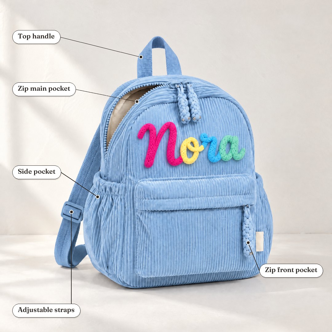 A blue corduroy backpack with the name Nora in rainbow letters, showing its zip pockets, side pocket, straps and top handle