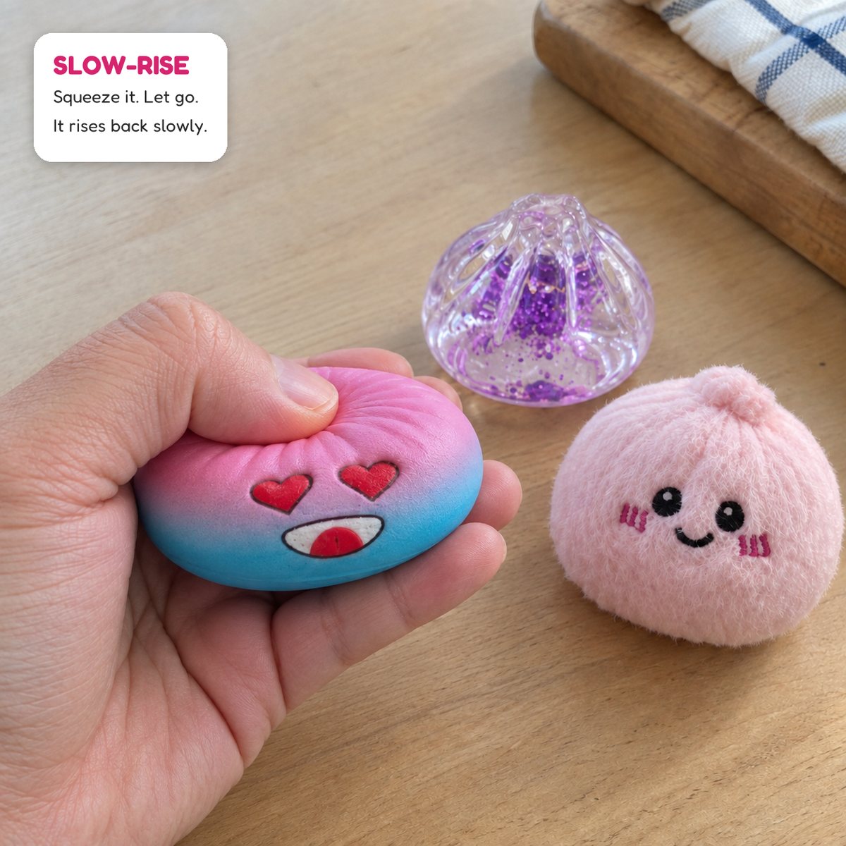 A hand squeezing a rainbow slow-rise dumpling, next to a glitter dumpling and a plush one