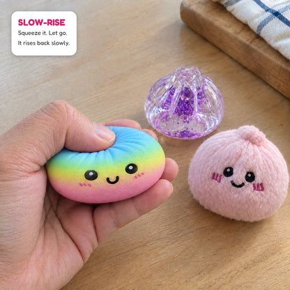 A hand squeezing a rainbow slow-rise dumpling, next to a glitter dumpling and a plush one